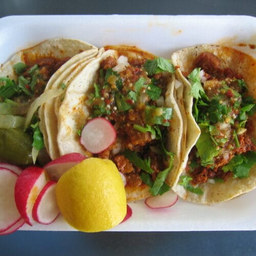 3 Hatch chiles and sweet potato tacos serviced with sliced radish and lemon wedge on a plate.